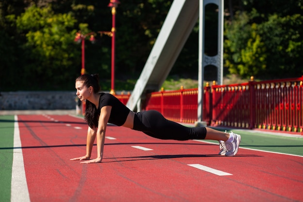 Young brunette athlete model doing plank exercise outdoor at the bridge