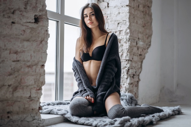 Young brunette in black underwear, knitted knee pads and cardigan