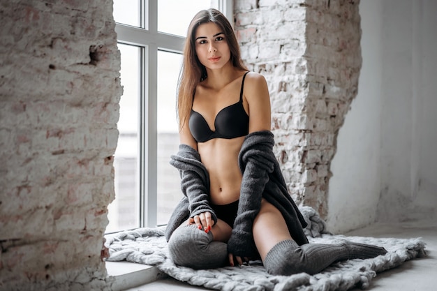 Young brunette in black underwear, knitted knee pads and cardigan