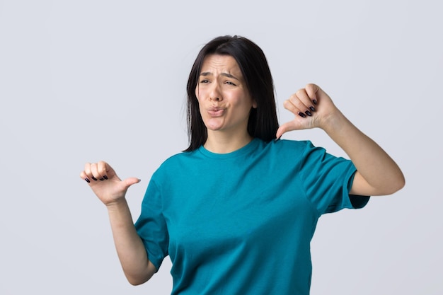 Young brunette in a blue tank top giving thumb down gesture looking with negative expression