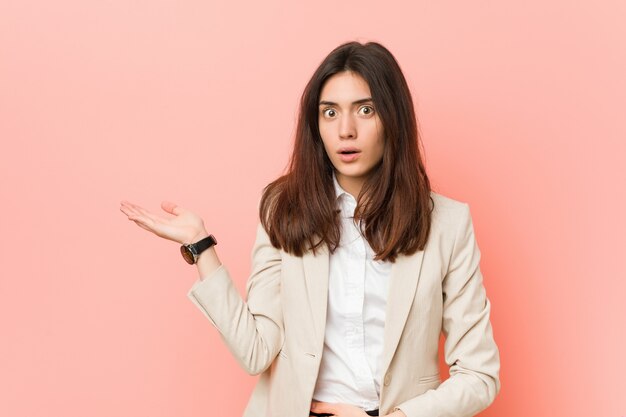 Young brunette business woman against a pink background impressed