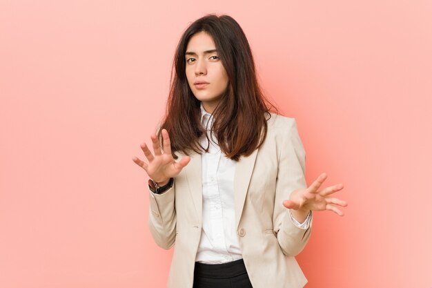 Young brunette business woman against a pink wall rejecting someone showing a gesture of disgust.