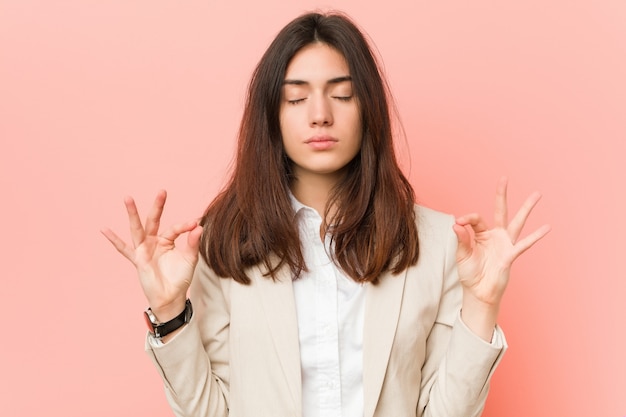 Foto la giovane donna castana di affari contro una parete rosa si rilassa dopo la dura giornata lavorativa, sta eseguendo lo yoga.