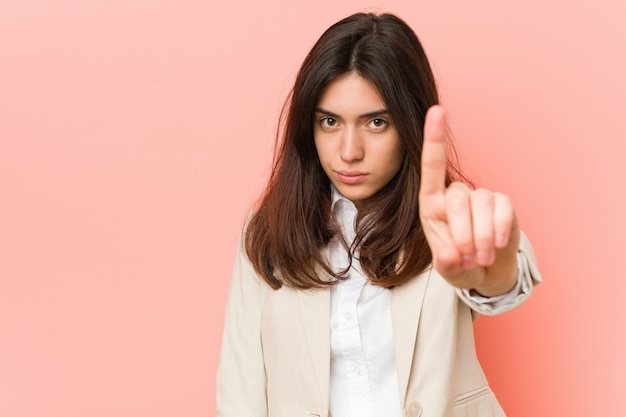 Young brunette business woman against a pink wall showing number one with finger.