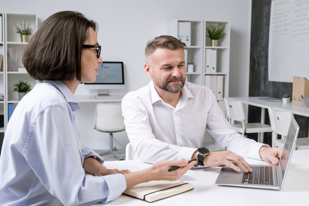 Young brunette businesswoman and her colleague discussing points of presentation while preparing for conference