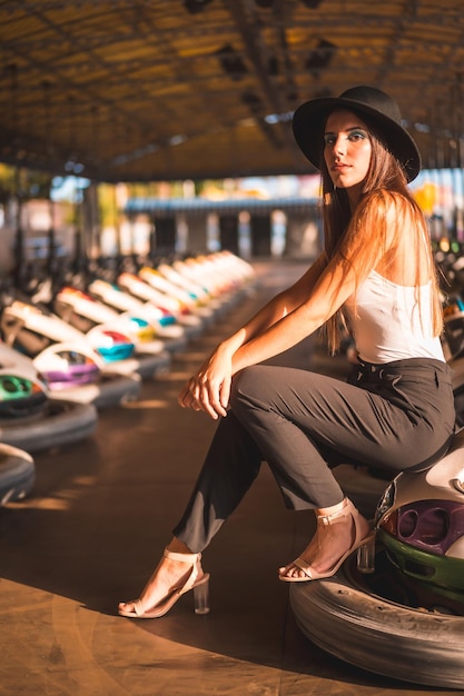 A young brunette Caucasian with heels pants and black hat in the bumper cars