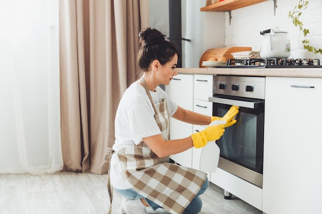 A young brunette cleans the kitchen a woman in gloves washes the stove the girl cleans the house