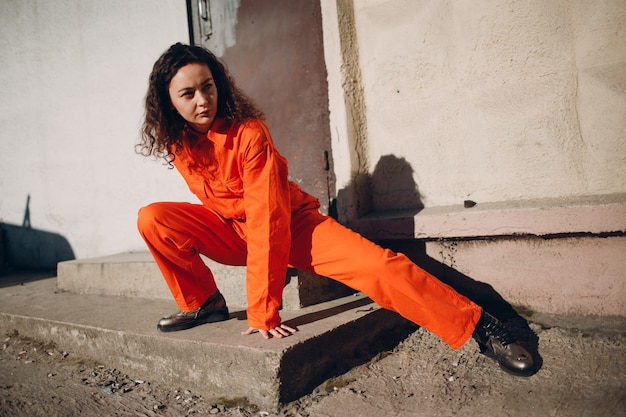 Young brunette curly woman in orange suit. Female in colorful overalls portrait.