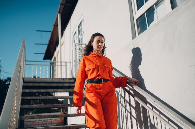 Young brunette curly woman in orange suit Female in colorful overalls portrait