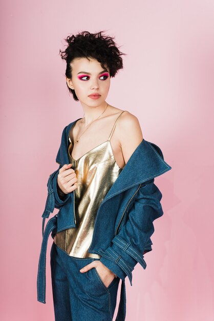 Young brunette in a denim suit and a gold top on pink