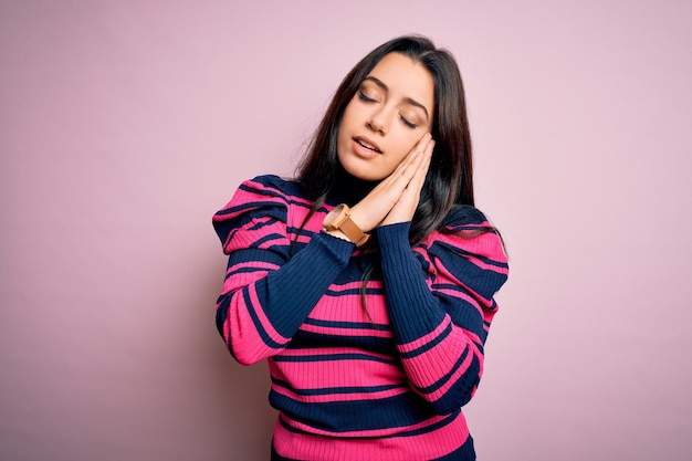 Young brunette elegant woman wearing striped shirt over pink isolated background sleeping tired dreaming and posing with hands together while smiling with closed eyes