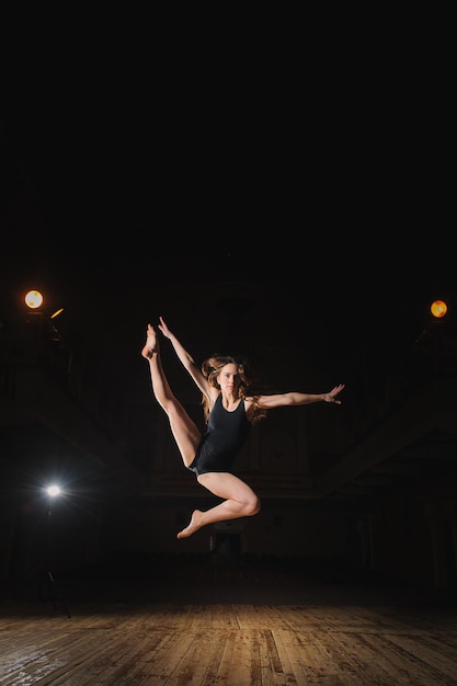 Young brunette female dancer doing split jump on stage