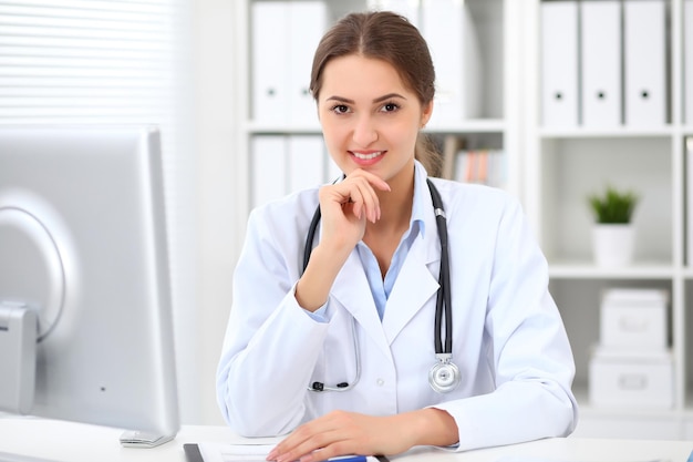 Young brunette female doctor sitting at the table and working at hospital office