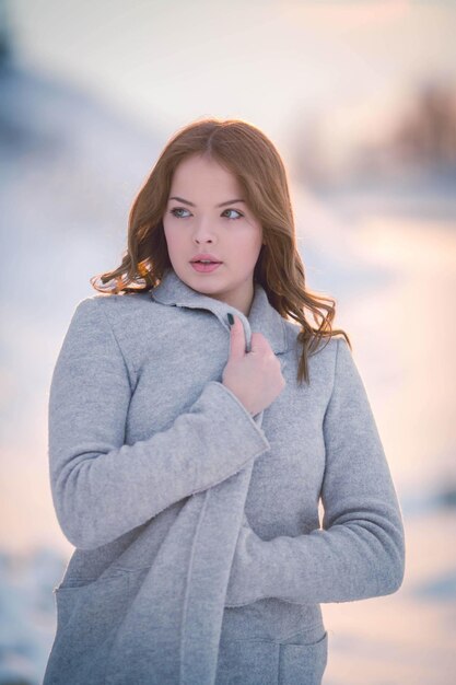 Young brunette female holding her coat and posing in a field covered in the snow in winter