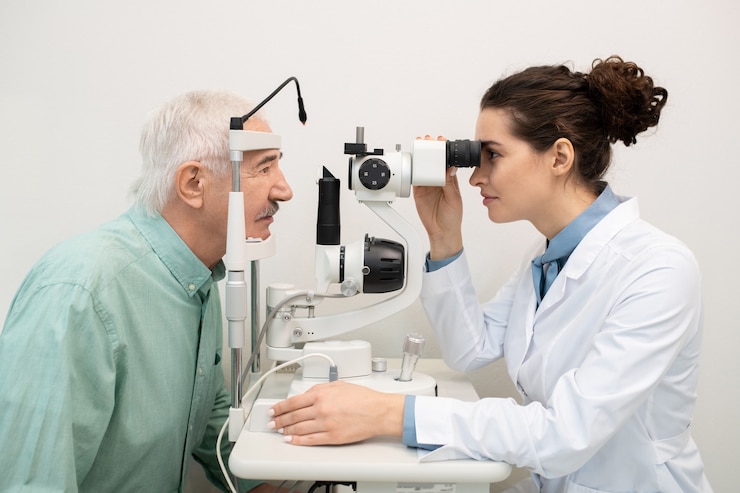 Photo young brunette female ophthalmologist sitting by medical equipment in clinics while testing eyesight of senior male patient in front of her