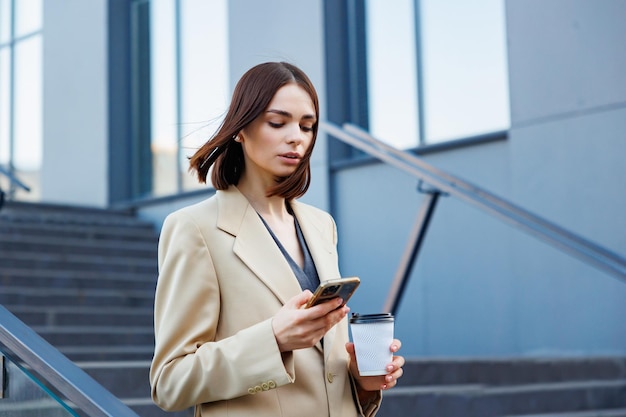 ビジネス センターのオフィス センターを背景に若いブルネットの少女 外出先で彼はスマートフォンからニュースを読みます