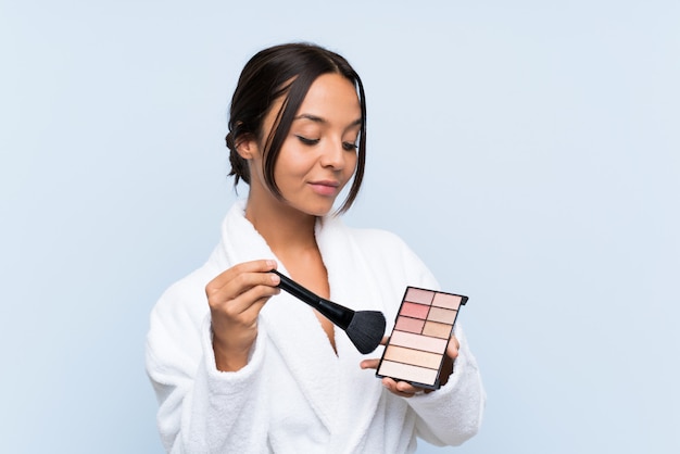 Young brunette girl in bathrobe with makeup over isolated blue wall