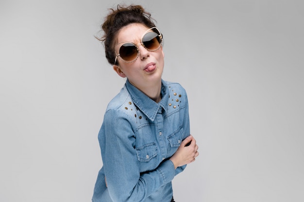 Young brunette girl in black glasses Cat glasses The hair is gathered in a bun The girl shows her tongue