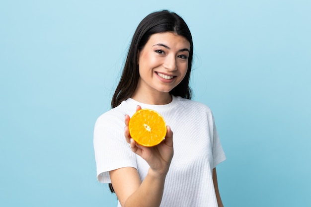 Young brunette girl over blue wall holding an orange