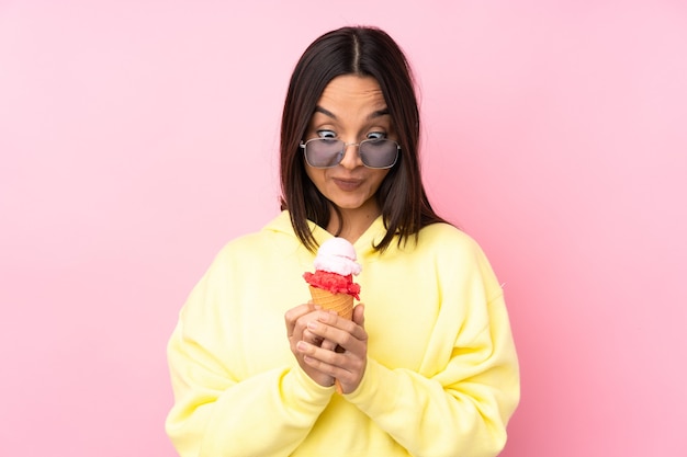 Young brunette girl holding a cornet ice cream over isolated pink wall scheming something