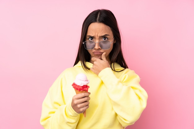 Young brunette girl holding a cornet ice cream over isolated pink wall thinking