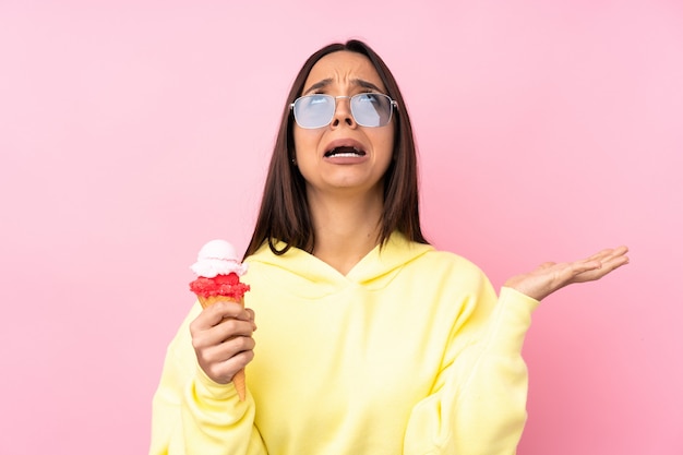 Young brunette girl holding a cornet ice cream over pink frustrated by a bad situation