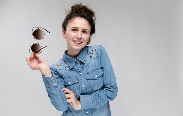 Young brunette girl holding glasses in her hand. Cat glasses. The hair is gathered in a bun.