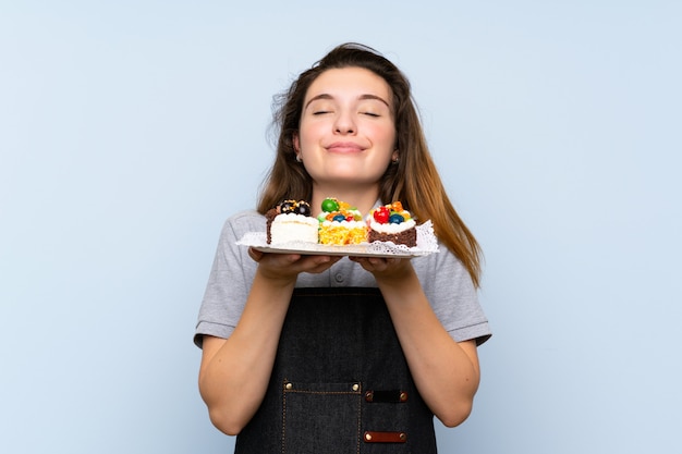 Young brunette girl holding mini cakes enjoying the smell of them