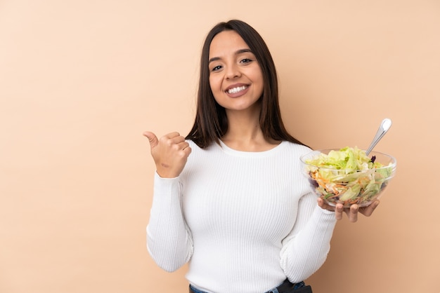 Young brunette girl holding a salad over isolated pointing to the side to present a product