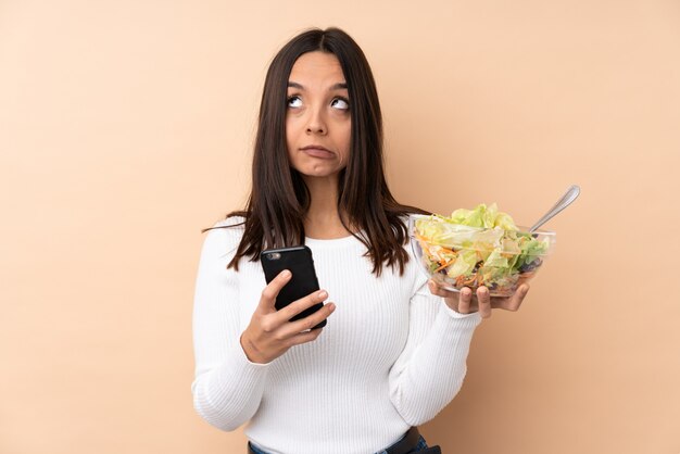 Young brunette girl holding a salad over isolated wall thinking and sending a message