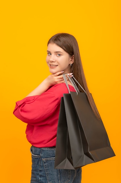 Young brunette girl holds black paper bag Portrait of customer with bag on bright yellow background Vertical frame