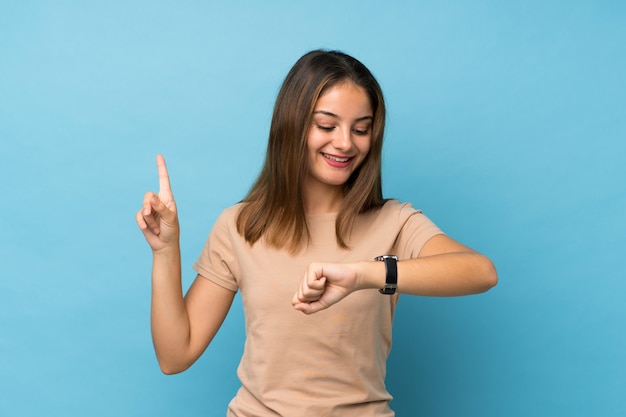 Giovane ragazza castana sopra il blu isolato che esamina l'orologio della mano