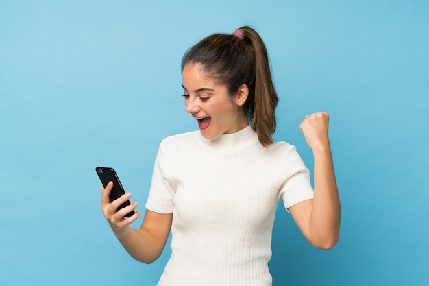 Young brunette girl over isolated blue using mobile phone