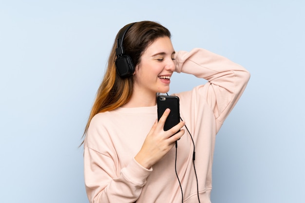 ヘッドフォンと歌で携帯電話を使用して分離の青い壁の上の若いブルネットの少女