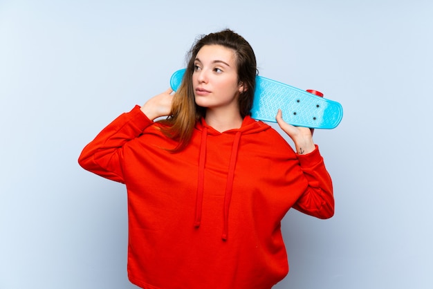 Young brunette girl over isolated blue wall with skate and looking side