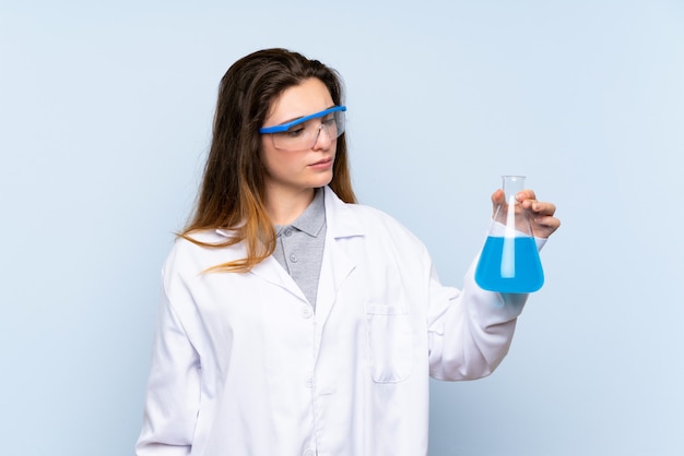 Young brunette girl over isolated blue with a scientific test tube