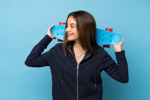 Young brunette girl over isolated blue with skate and looking side