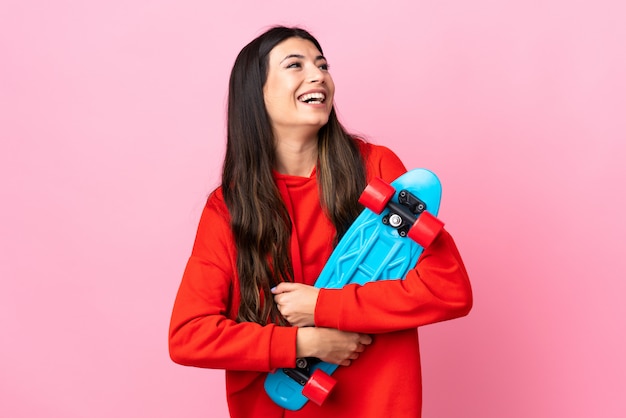 Young brunette girl over isolated pink wall with a skate with happy expression