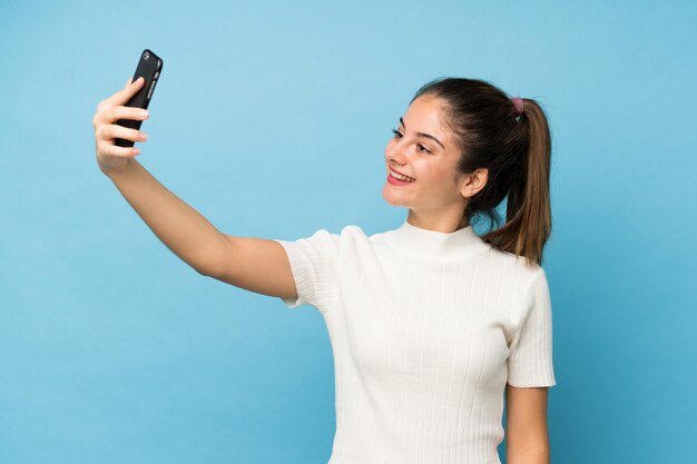 Young brunette girl over isolated  taking a selfie with the mobile