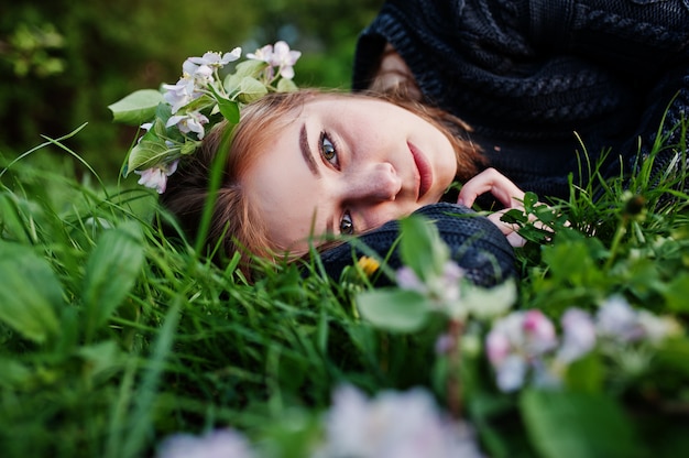 Young brunette girl lying on green grass with branches of blossom tree.