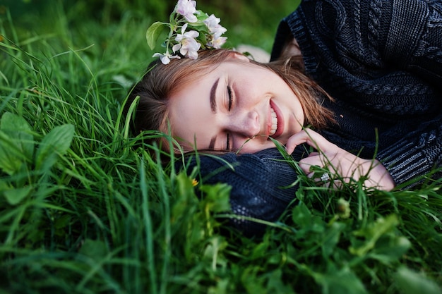 Young brunette girl lying on green grass with branches of blossom tree