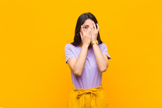 young brunette girl peeking or spying with eyes half-covered with hands