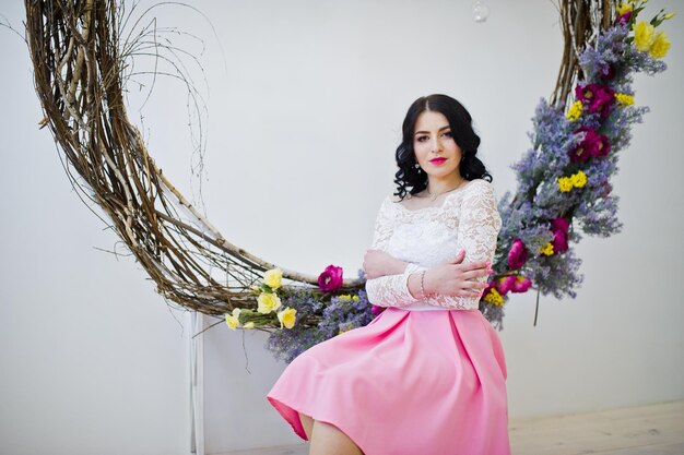 Young brunette girl in pink skirt and white blouse posed indoor against large decorated wreath