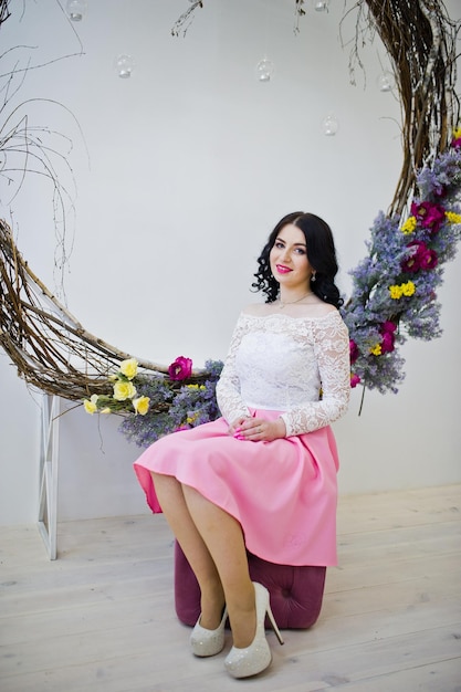 Young brunette girl in pink skirt and white blouse posed indoor against large decorated wreath