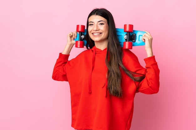 Young brunette girl over pink wall with a skate with happy expression