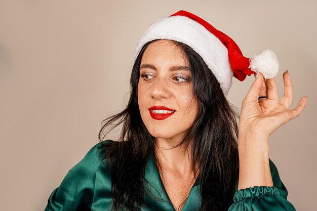 Foto una giovane ragazza bruna e un cappello rosso dell'aiutante di babbo natale pubblicità di natale le vacanze invernali capodanno la ragazza di babbo natale festeggia il natale