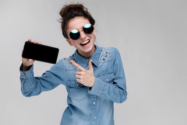 Young brunette girl in round glasses. Hairs are gathered in a bun. Girl with a black phone.