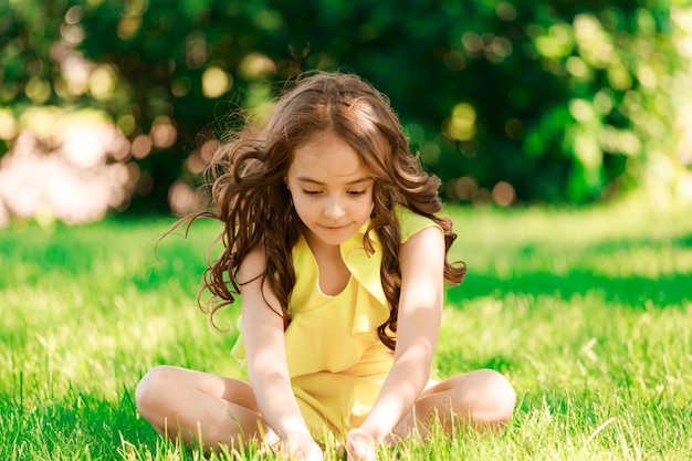 公園の芝生の上に座っている若いブルネットの少女。高品質の写真