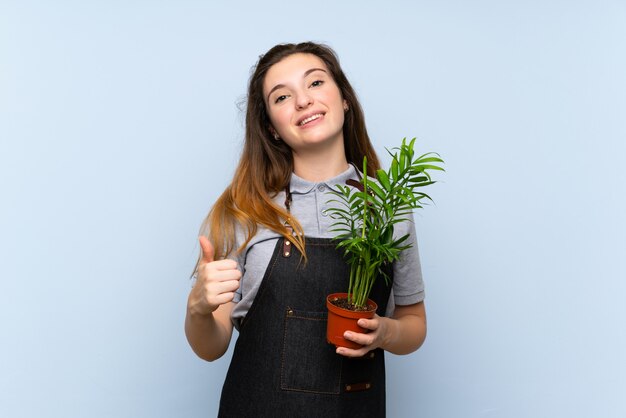 Young brunette girl taking a flowerpot and with thumb up