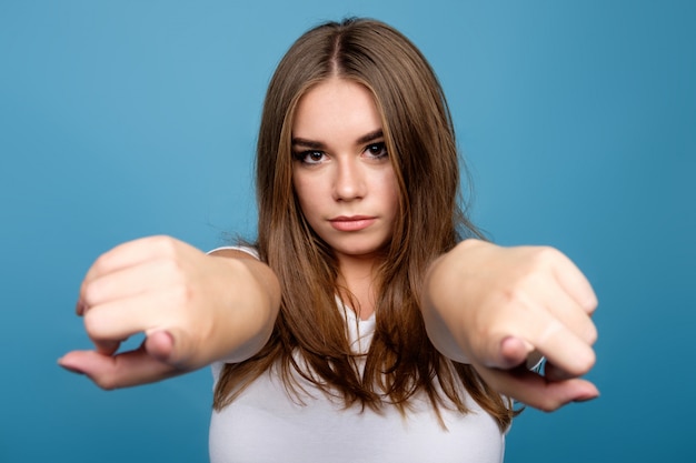 Young brunette girl in white t-shirt pointing forward with forefingers, blue background